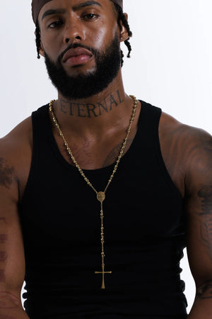 Man wearing the gold filled rosary bead necklace with a black vest, cross hanging mid chest