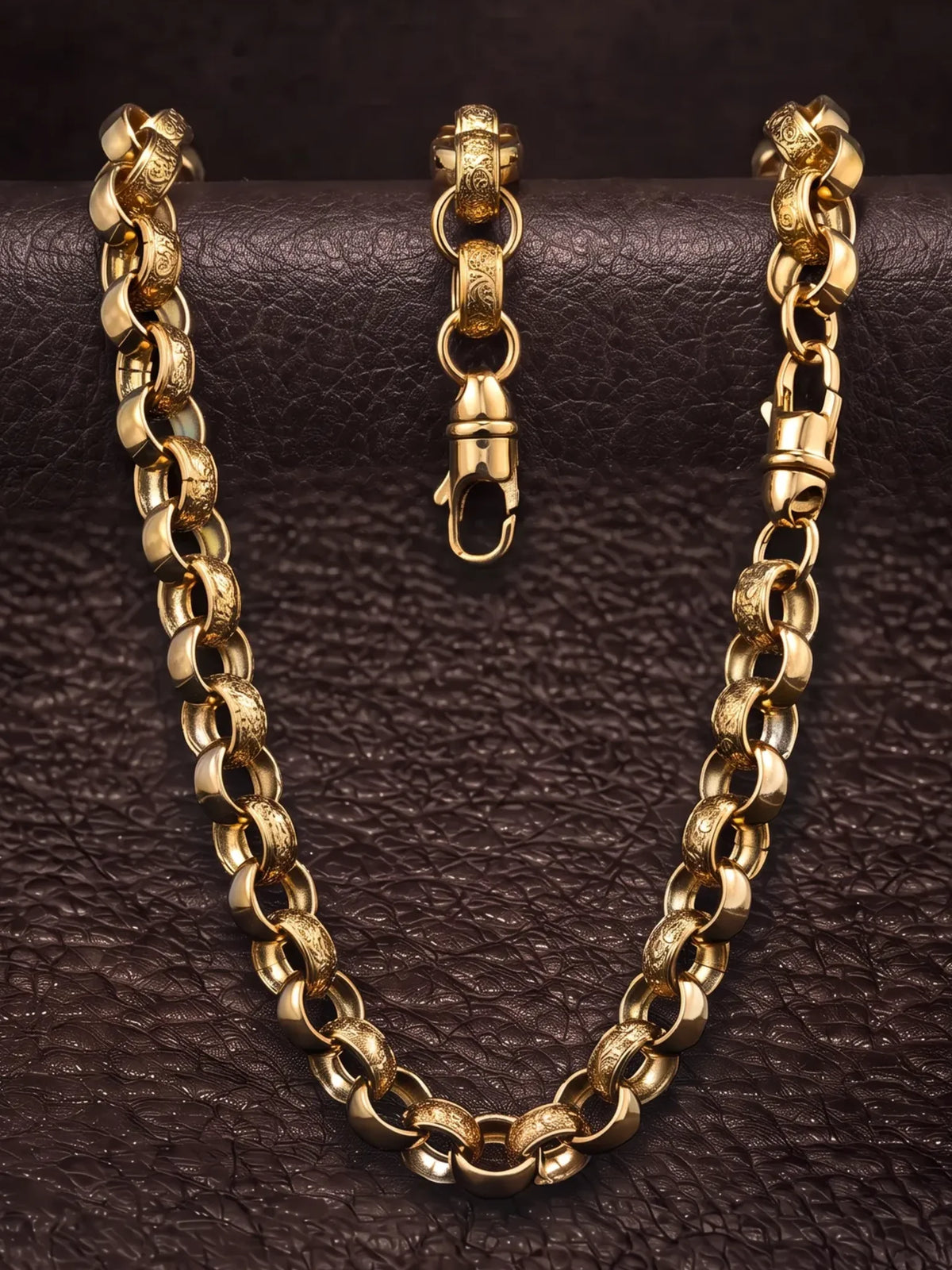 The 15mm patterned belcher chain laid over dark leather with the chunky lobster clasp open
