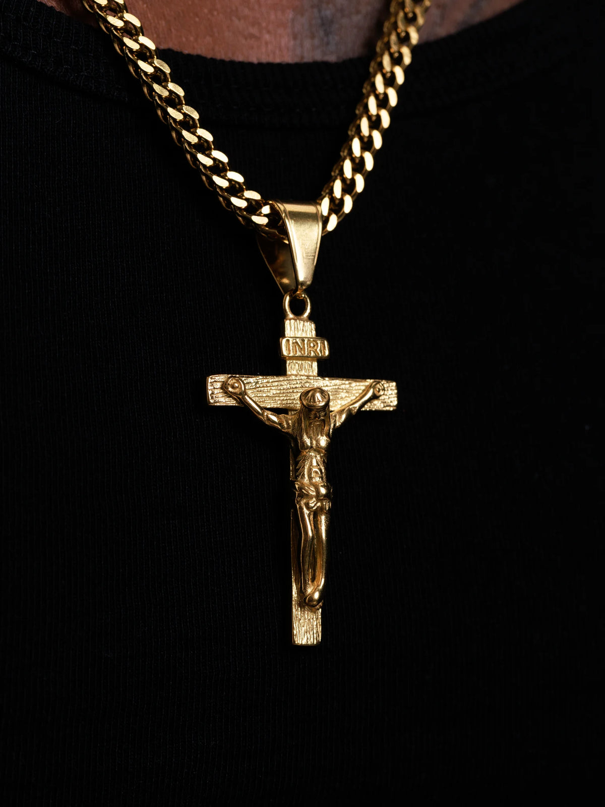 Close up of the gold filled INRI crucifix pendant and 4mm Franco chain links against a black top