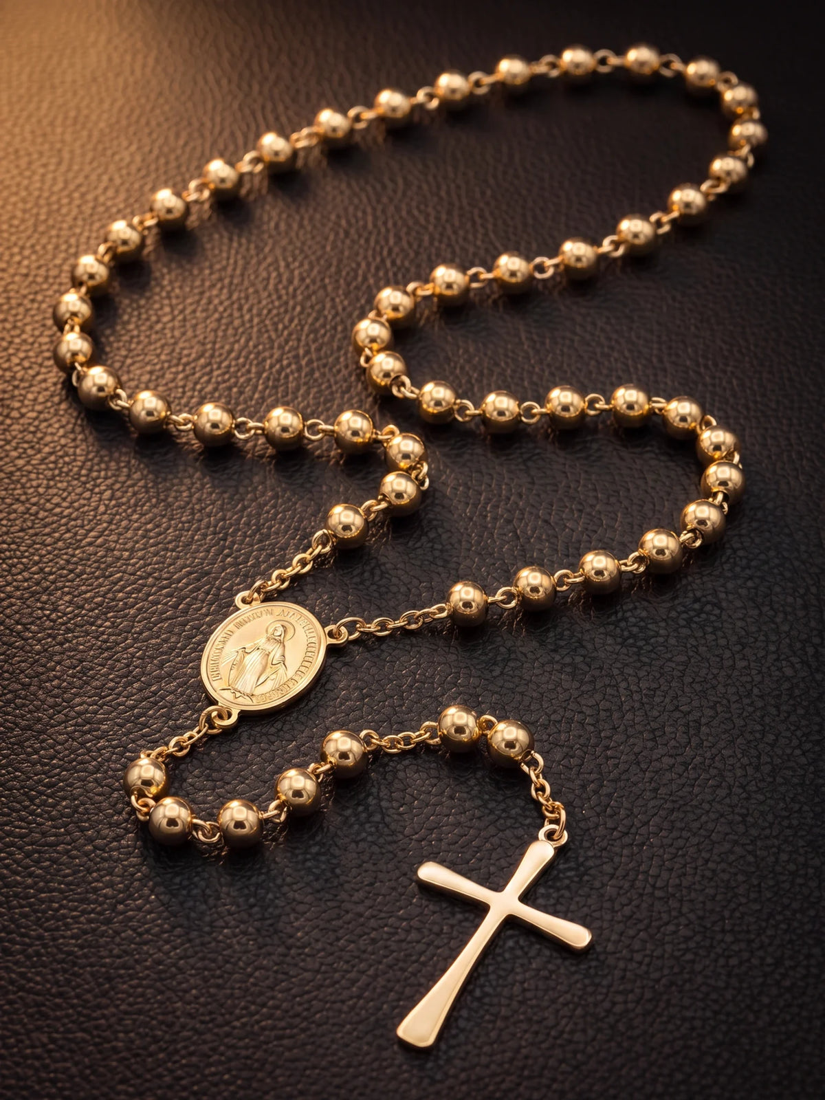 Gold filled rosary bead necklace laid out on dark leather showing the beads, centre medal and cross