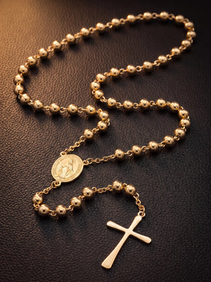 Gold filled rosary bead necklace laid out on dark leather showing the beads, centre medal and cross