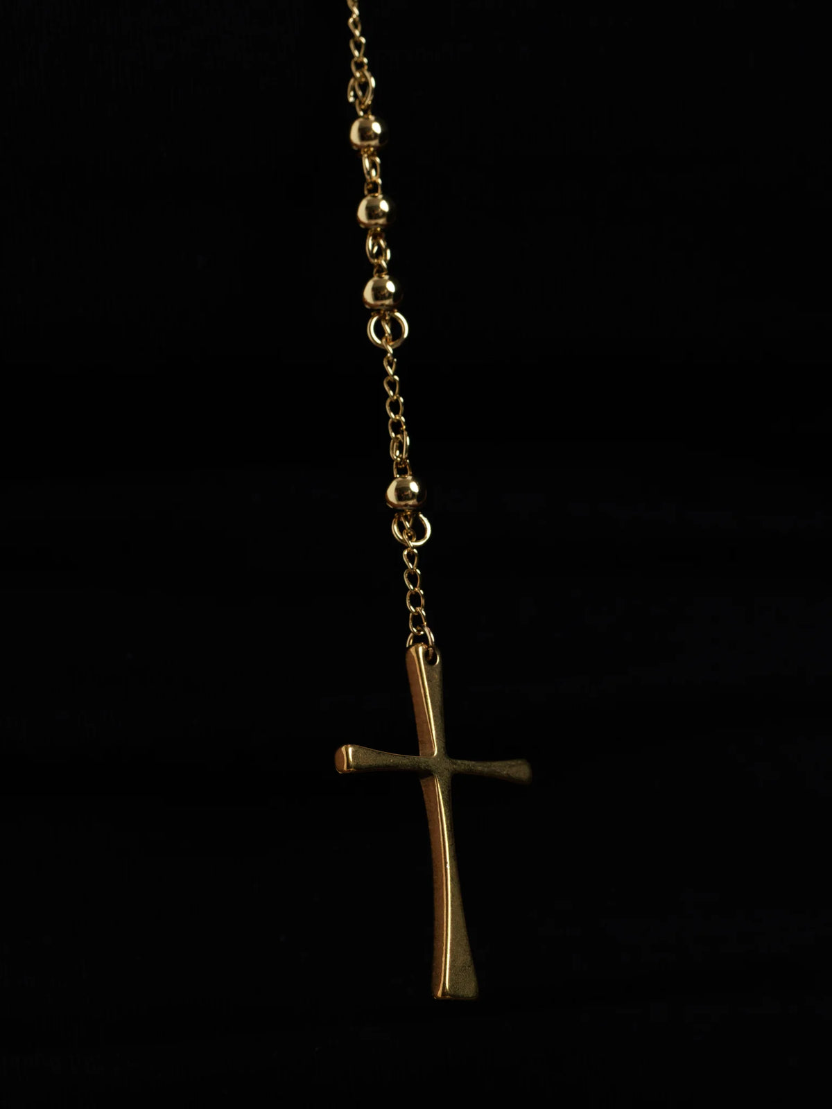 Detail of the tapered cross at the end of the rosary bead drop against a dark background