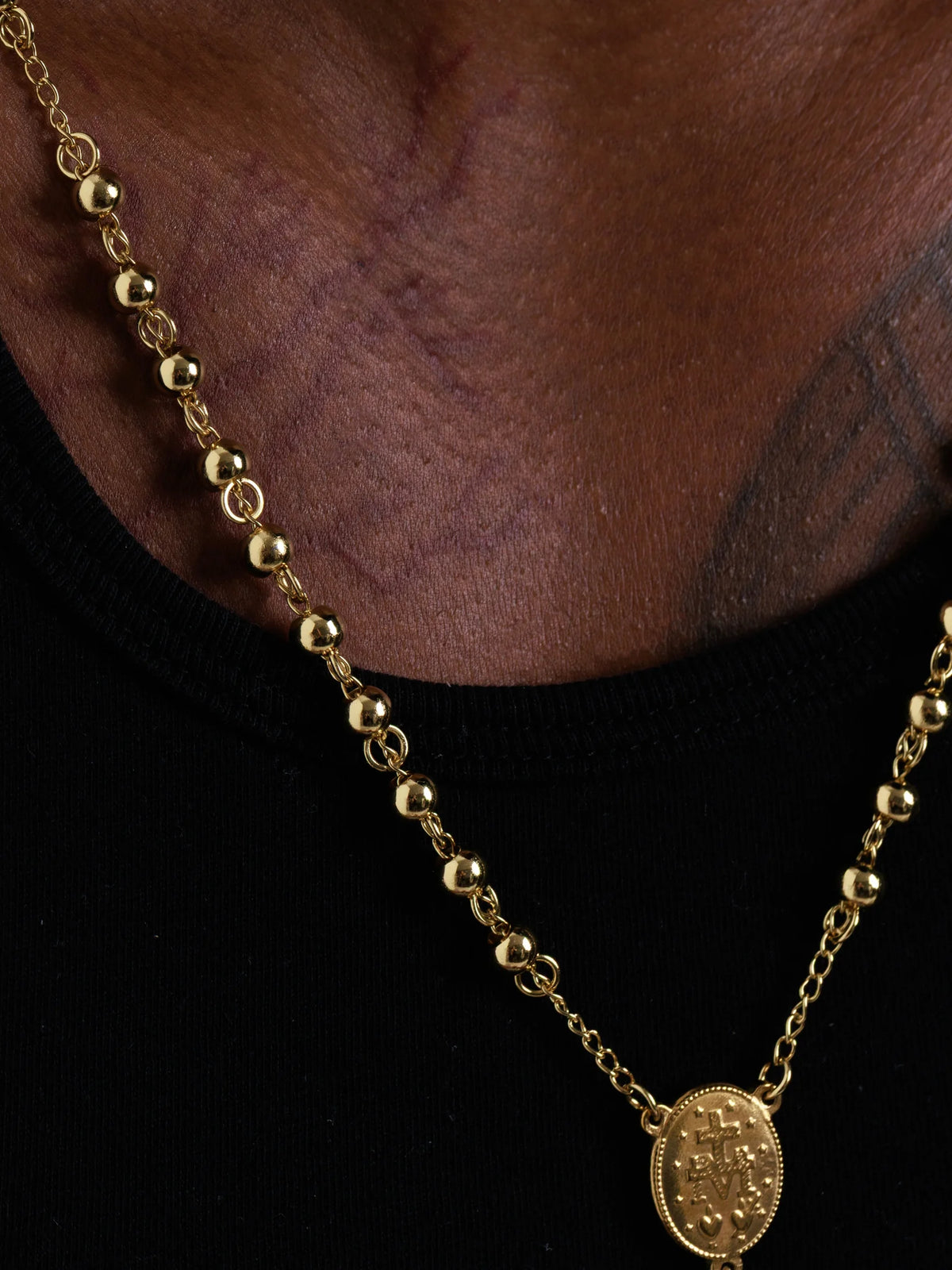 Close view of the polished gold beads and the oval centre medal on the rosary necklace