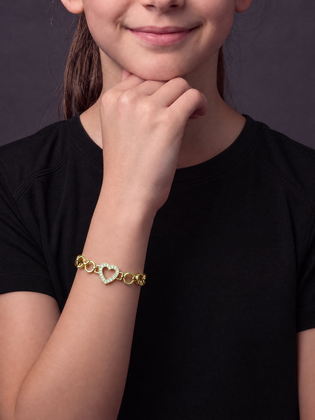 Girl resting her chin on her hand wearing the Girls Love Heart Charm Belcher Bracelet Gold Filled